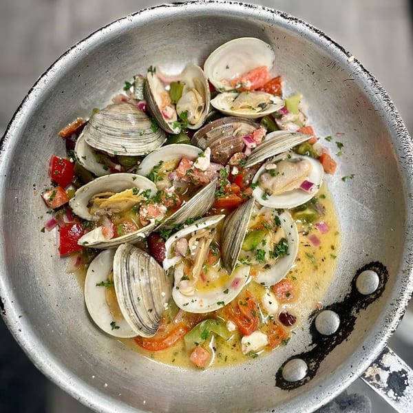 Steamed clams in a pan with broth, diced tomatoes, onions, and herbs.